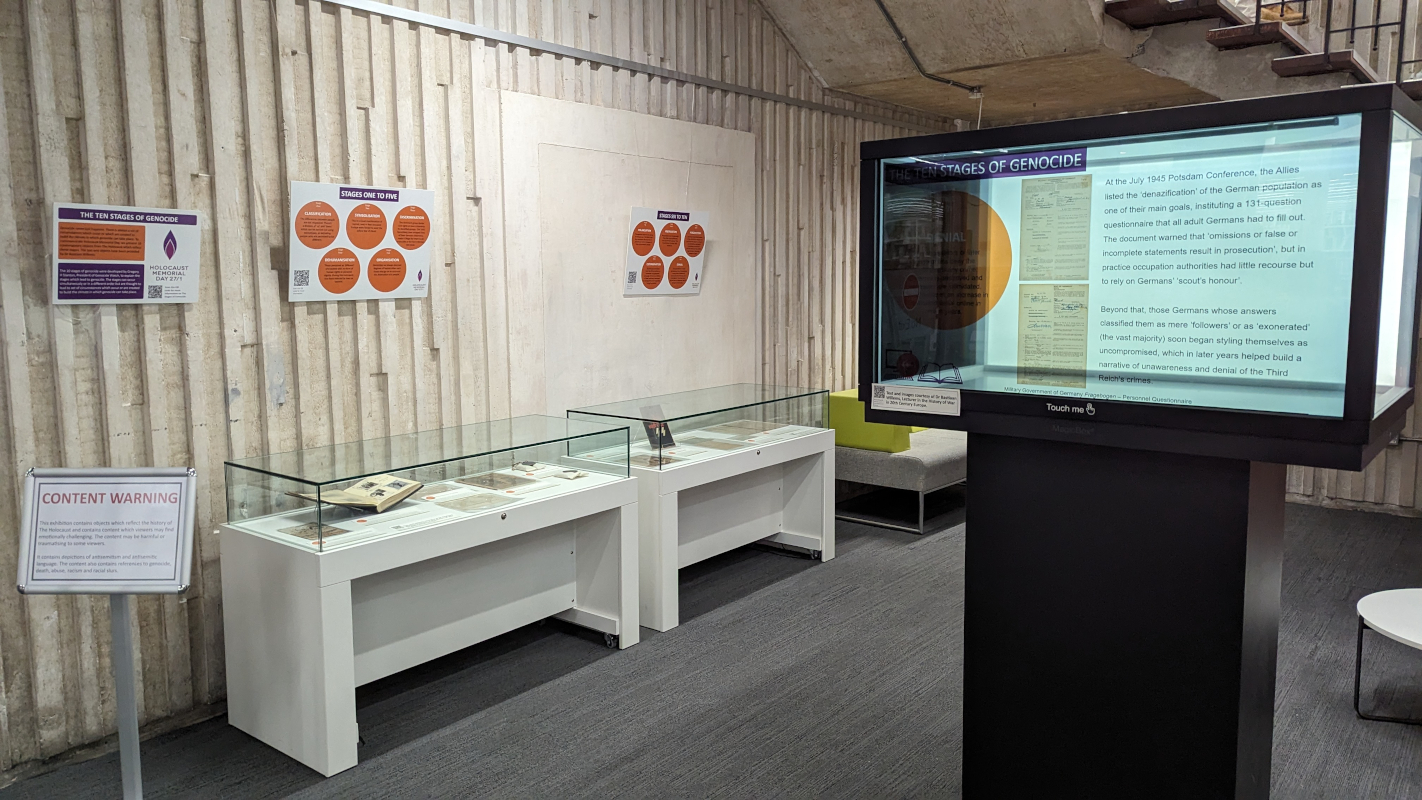 Holocaust Memorial Day 2024 exhibition featuring boards and objects in cabinets.