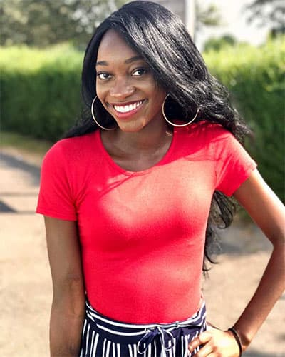 A black woman wearing a bright red top and smiling at the camera on a sunny day.