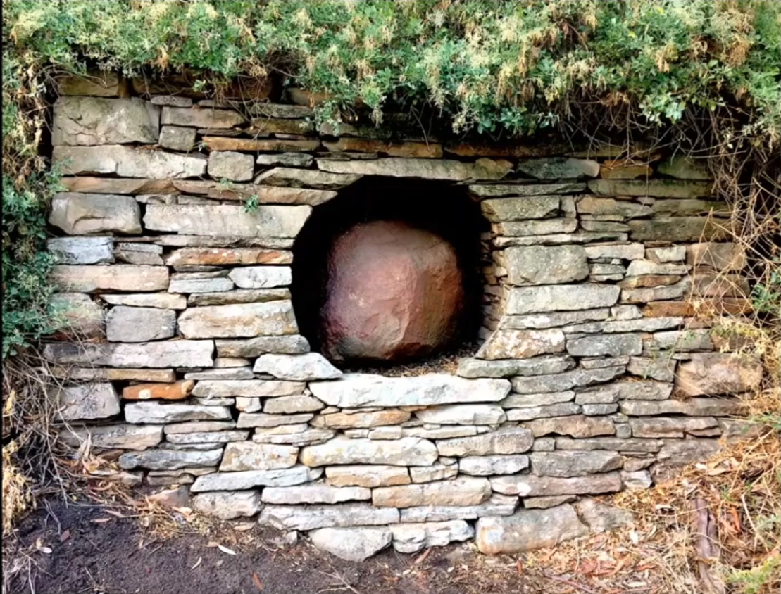 A dry-stone wall build with a sculptural circular hole in the middle, housing a large rock.