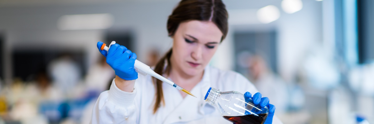 Student in a white lab coat at a laboratory bench using a pipette on a coloured liquid