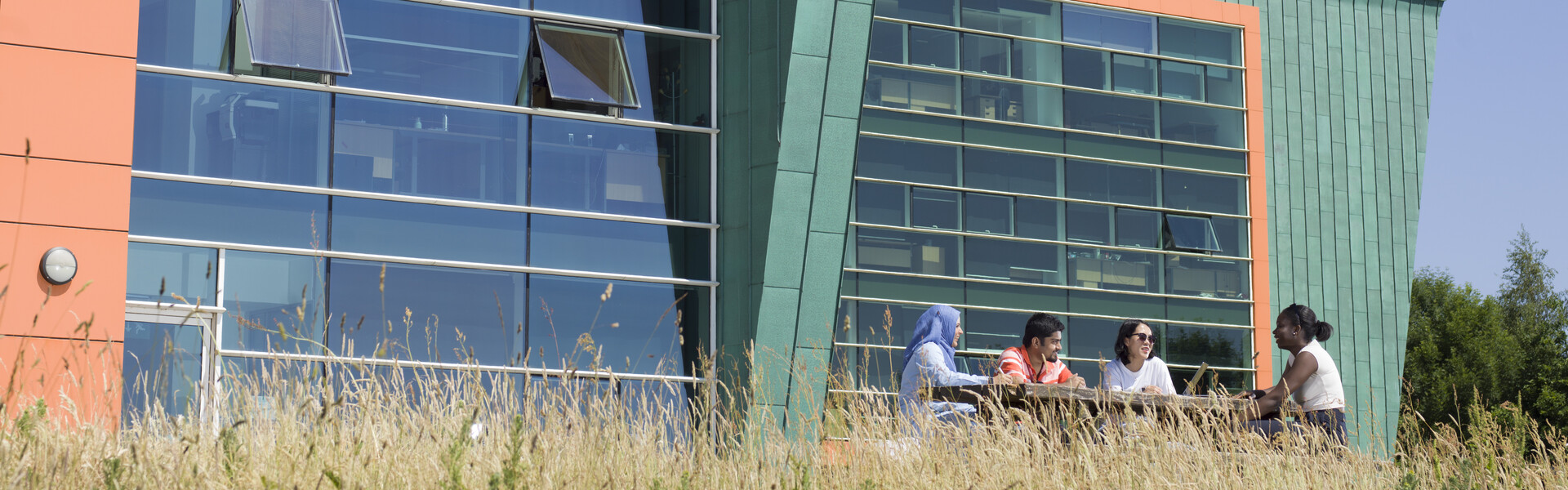 Students sat at table in front of Infolab, a green building with large windows