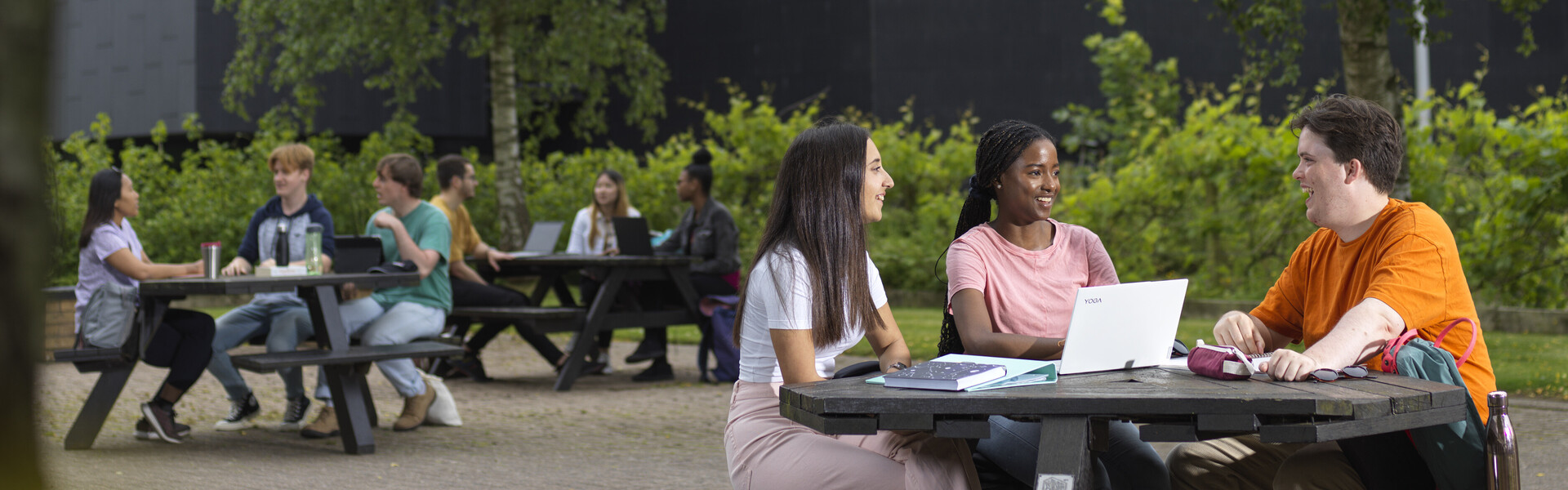 Students on a bench on laptops surrounded by greenery