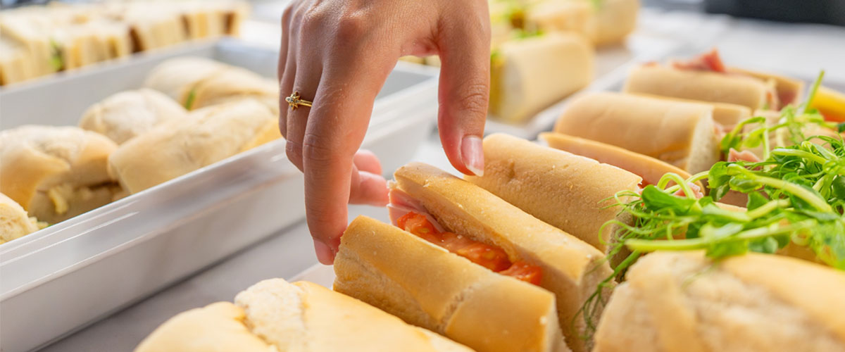 Hand coming down to pick up a baguette from a tray of baguettes