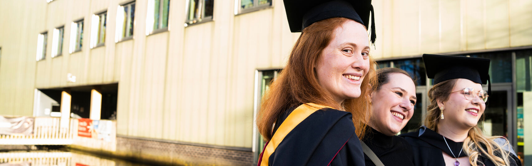 Three students in graduation robes outside of the LICA building.