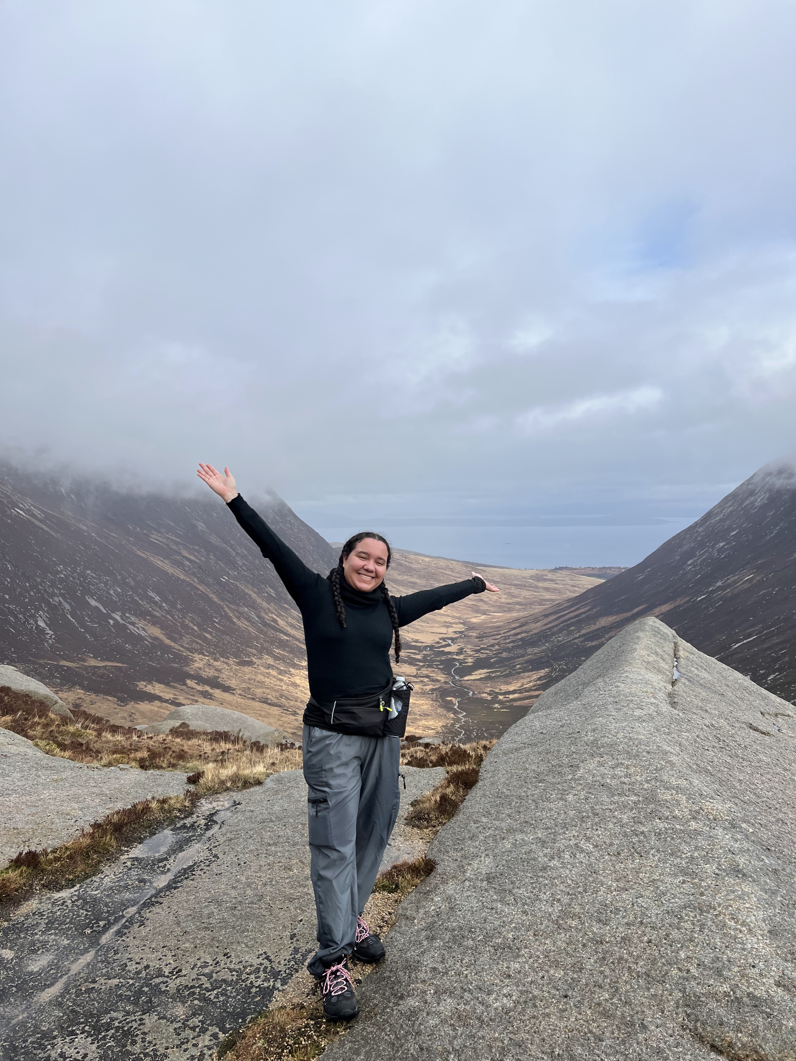 Image of student Lyea with arms out smiling atop a mountain