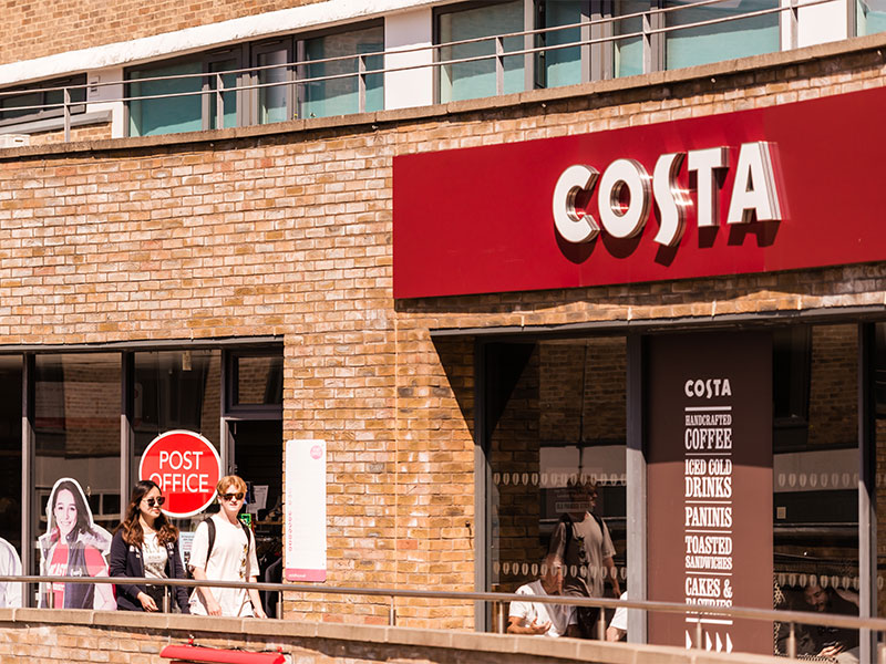 Two students walking past Costa Coffee located within Edward Roberts Court, Lancaster University