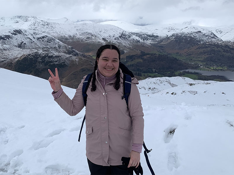 Student Lyea standing on a snowy hill with snowy mountains in the distance.