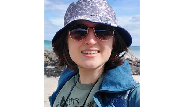 Image of student Anna in a bucket hat and sunglasses, smiling at the camera. 