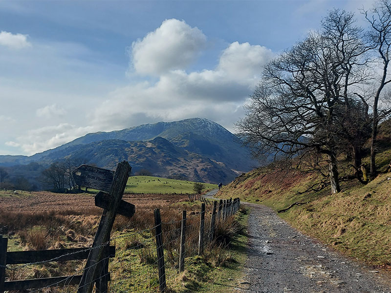 A sunny day in Langdale valley, footpath with sign in foreground and hills in background.