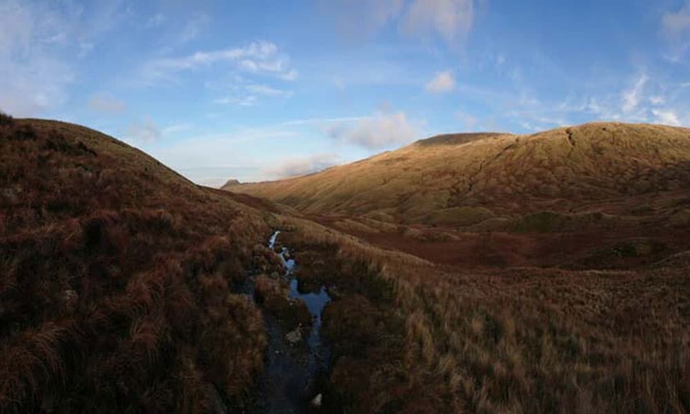 view of a fell in the sunshine with a stream running through