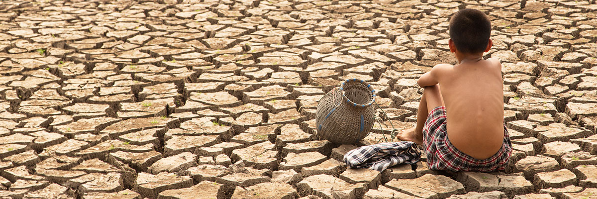 Young boy sitting on dry cracked ground caused by drought.