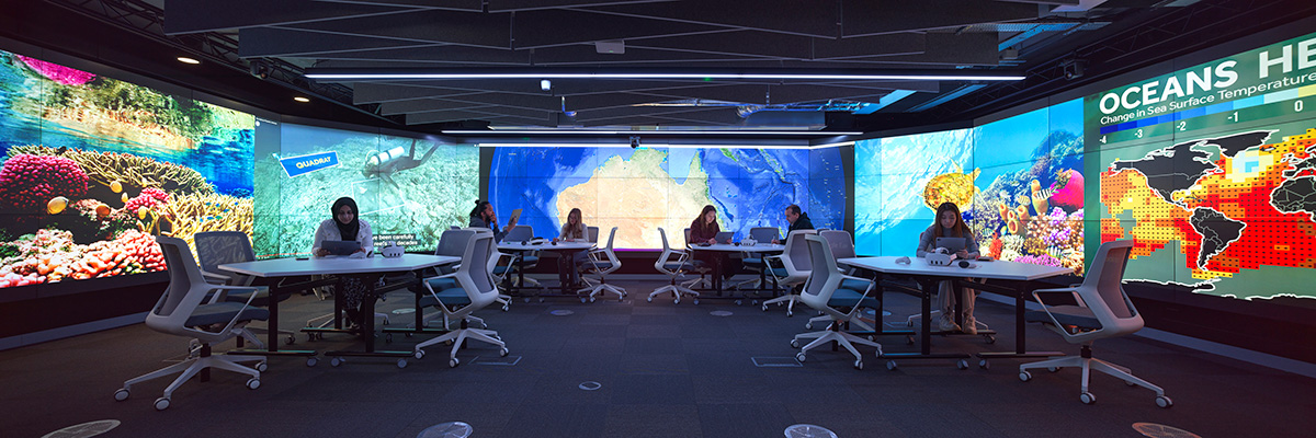 A darkened room with people at tables surrounded by giant multi-panel video displays