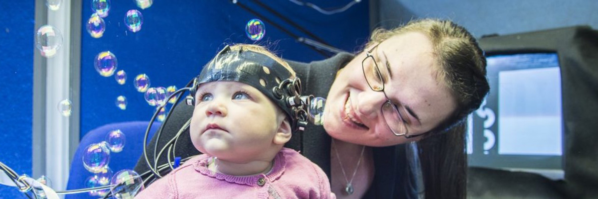 A baby in an EEG cap and a researcher watching some bubbles in the lab