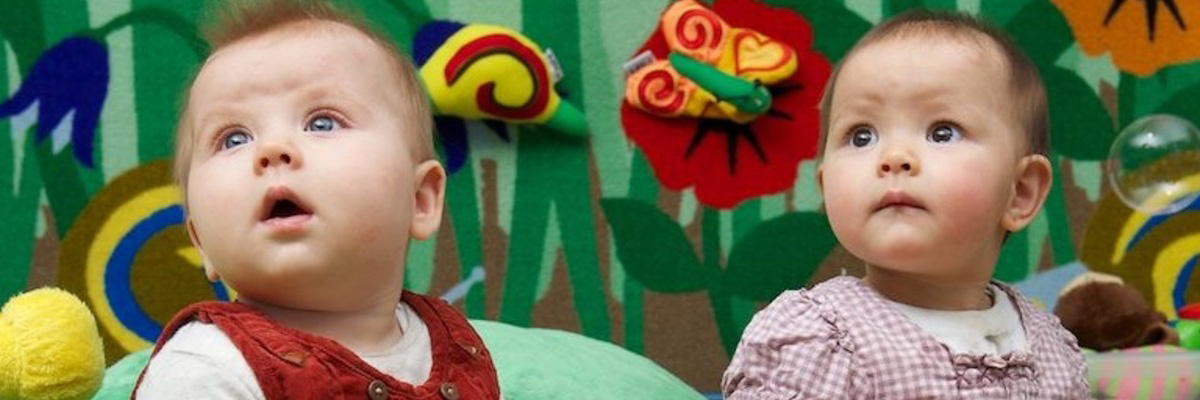 Two babies sat against the colourful wall in the BabyLab