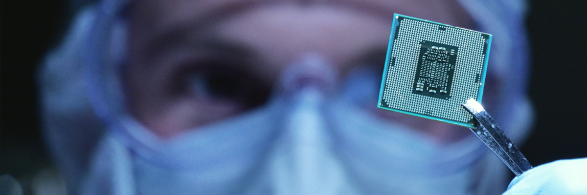 A person in PPE holding up a circuit board with a pair of tweesers