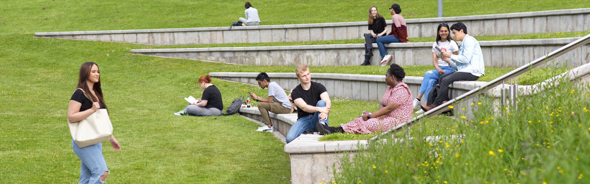 Three students walk across Lancaster University's main square on a sunny day