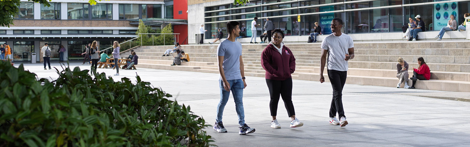 Three students walk across Lancaster University's main square on a sunny day