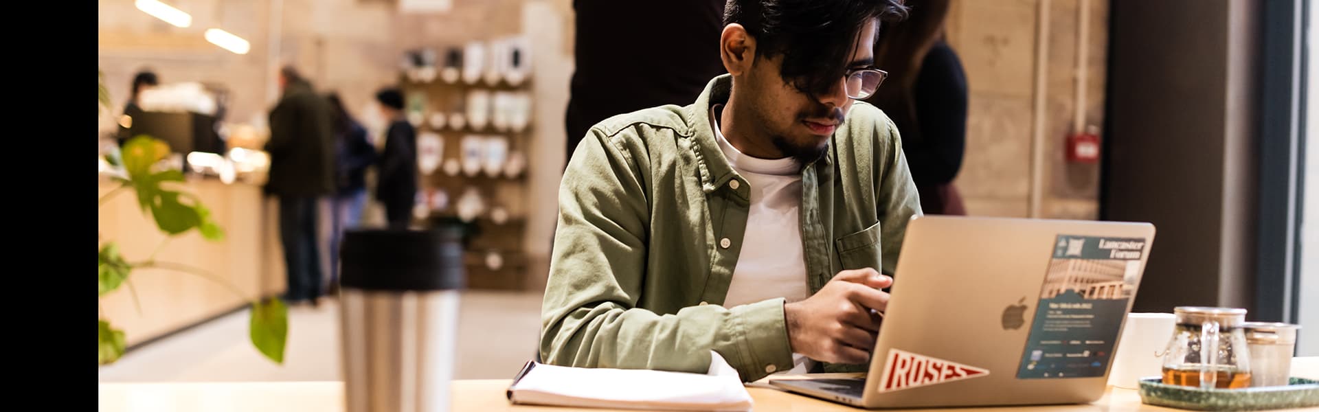 A student sitting at a cafe table looking at a laptop