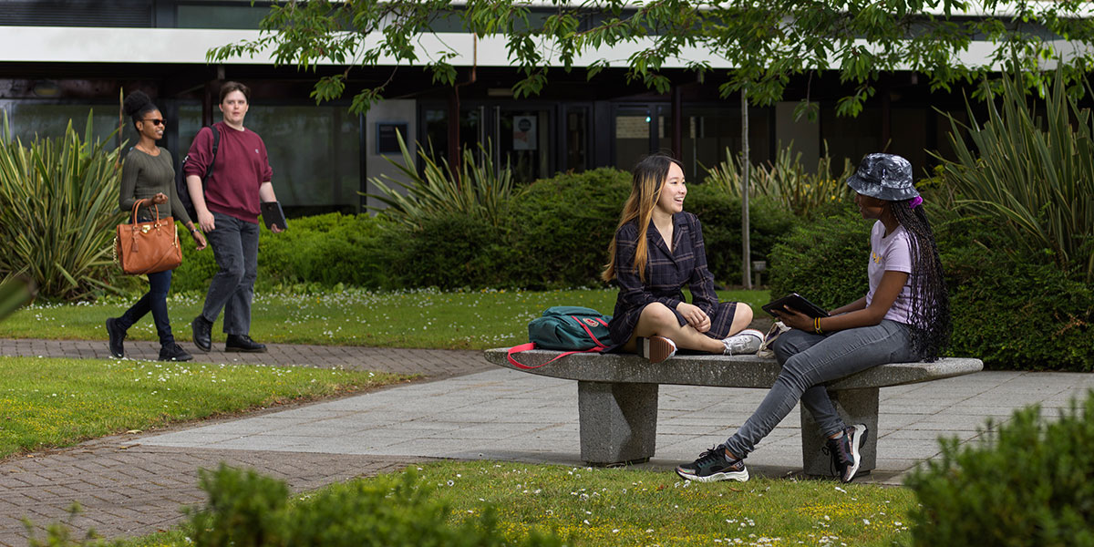 Students chat and relax on Lancaster's green campus on a sunny day