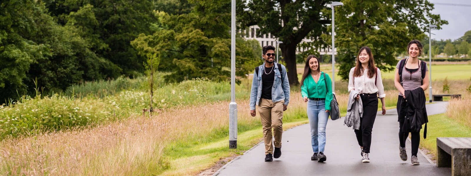 Students walking along a path surrounded by green spaces. Behind them, there is a modern building.