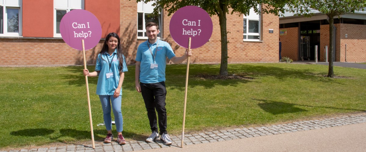 Two student ambassadors hold signs for an open day.