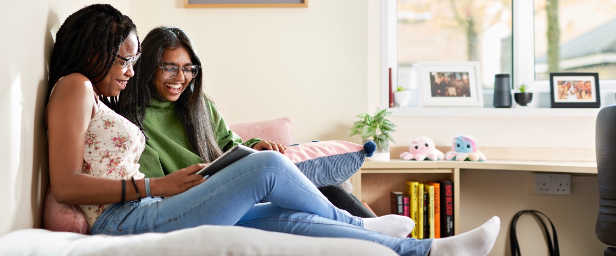 Two students sit on a bed and read