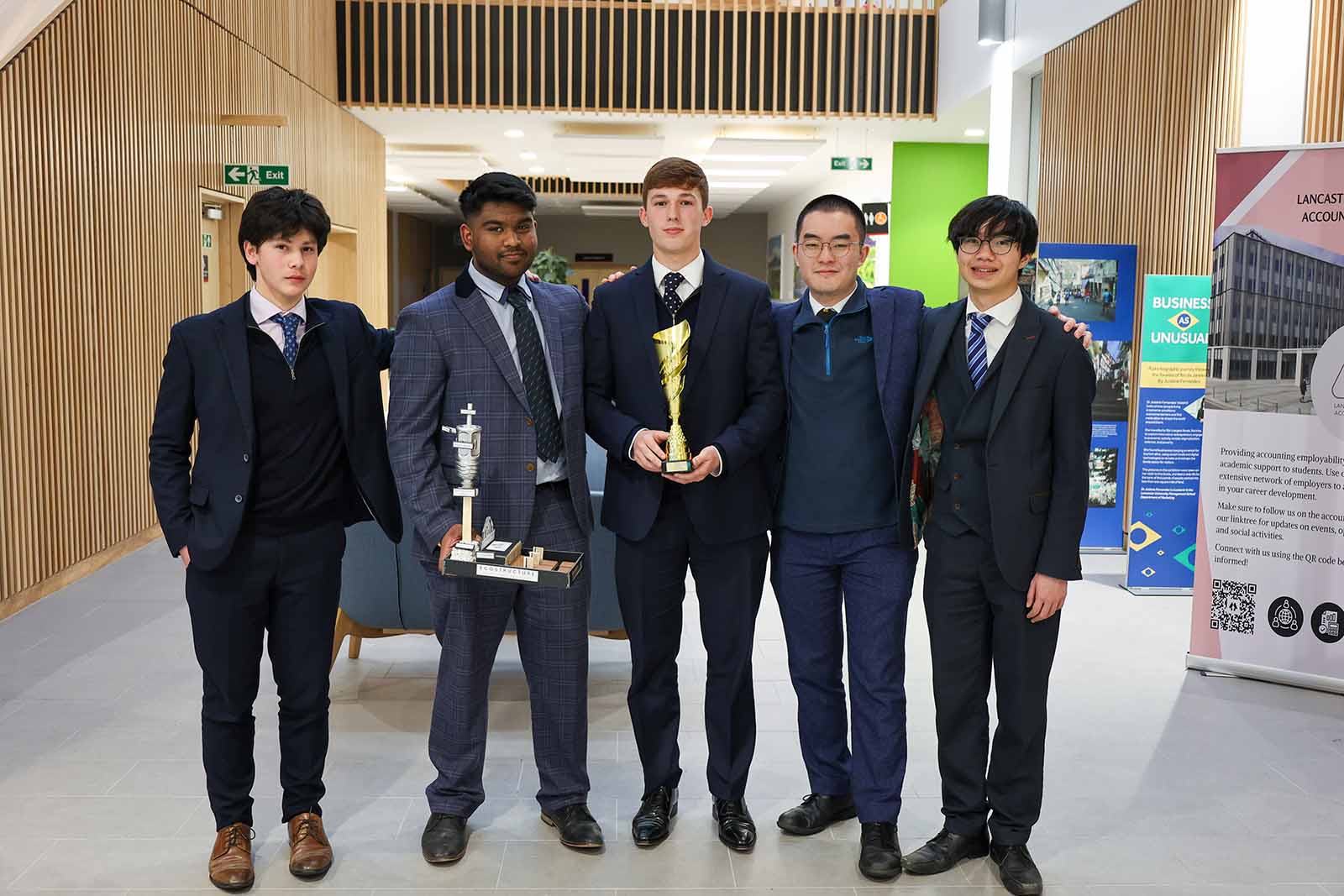 Five students in a row, one holding a golden trophy