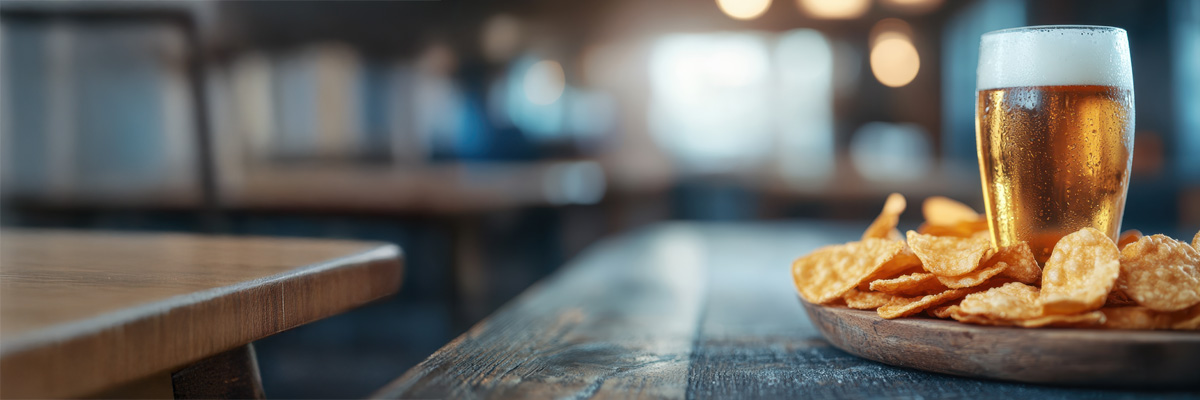 A pint of beer and bowl of crisps on a wooden table