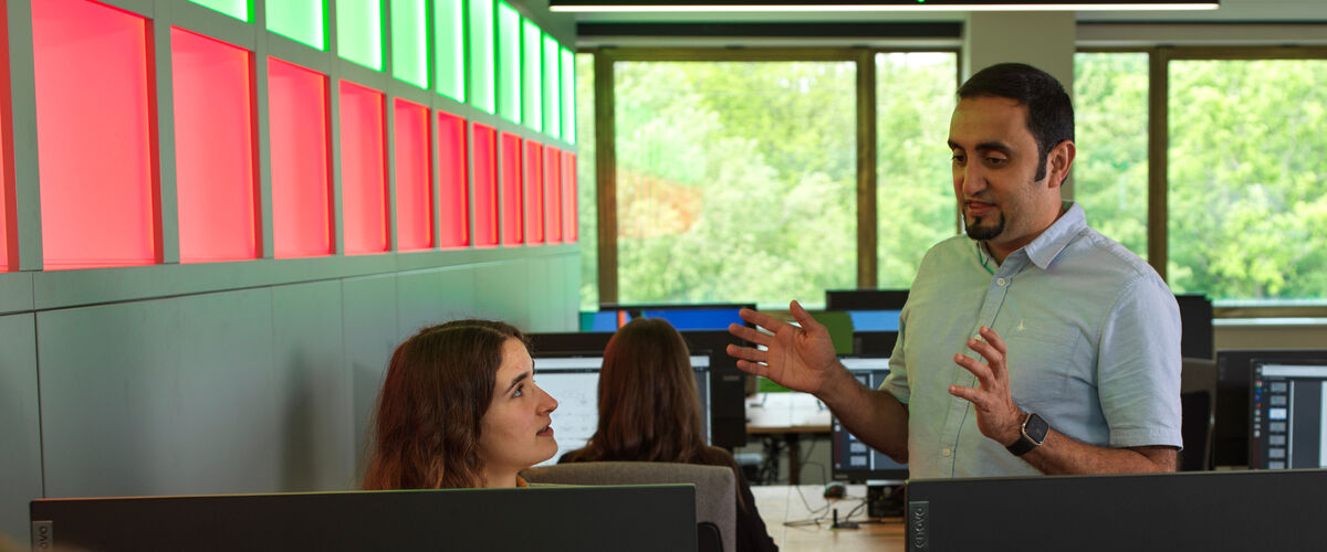 Lecturer in a computer lab speaking with a student