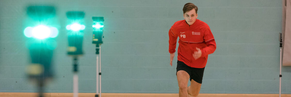 Sports and Exercise Science student in red sportswear running through light gates in a sports hall