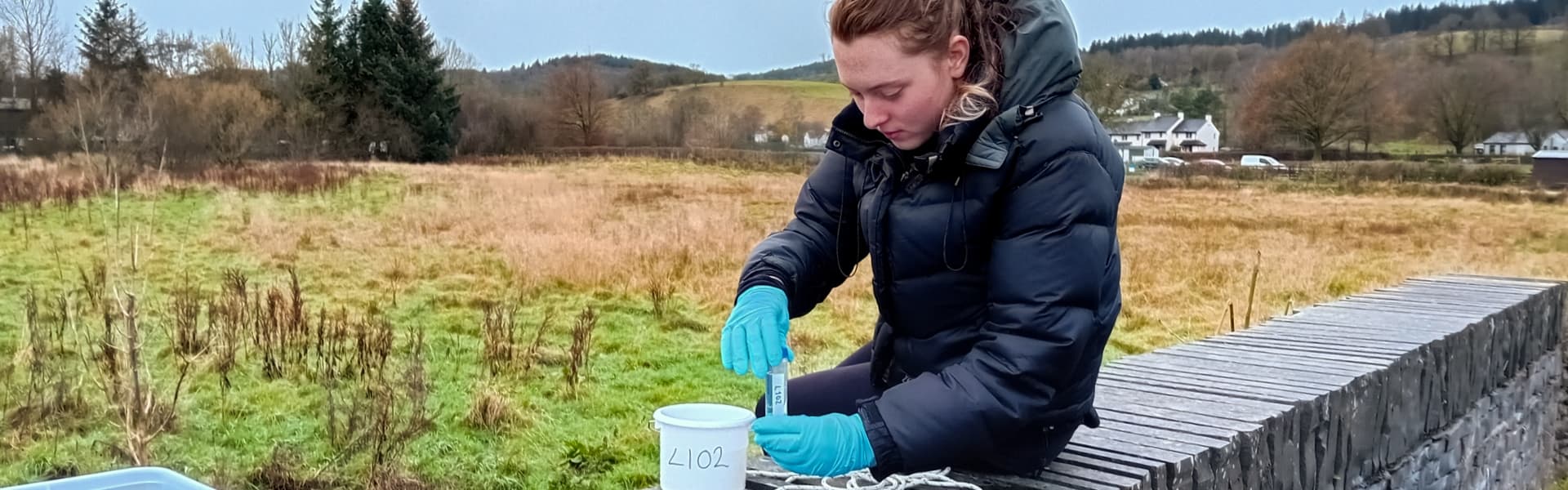 A person in an anorak takes a water sample in Hawkshead