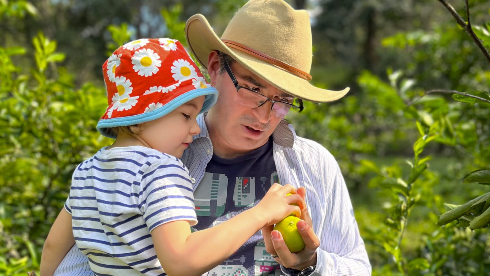 Dr Allan Discua Cruz holds a small child in one arm and an apple in the other hand. They are standing in an orchard.