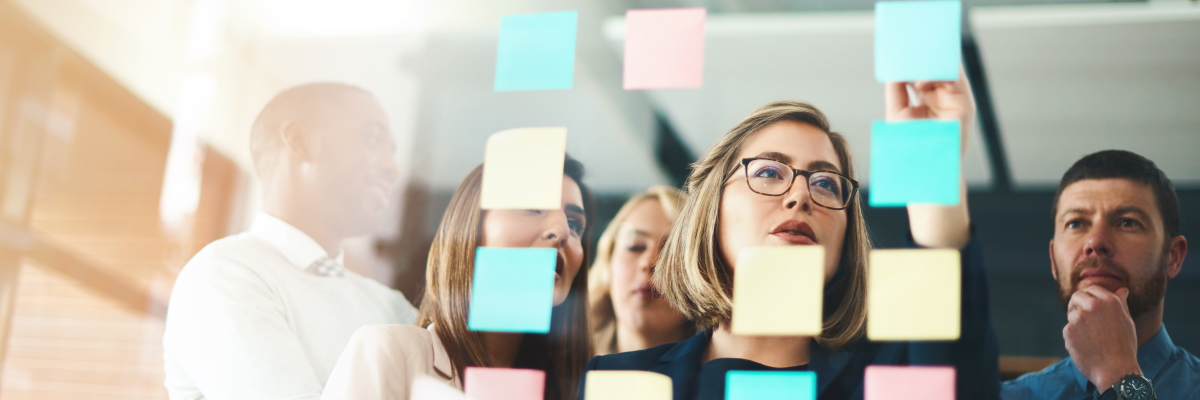 A group of people looking at colourful post-it notes arranged on a transparent wall.