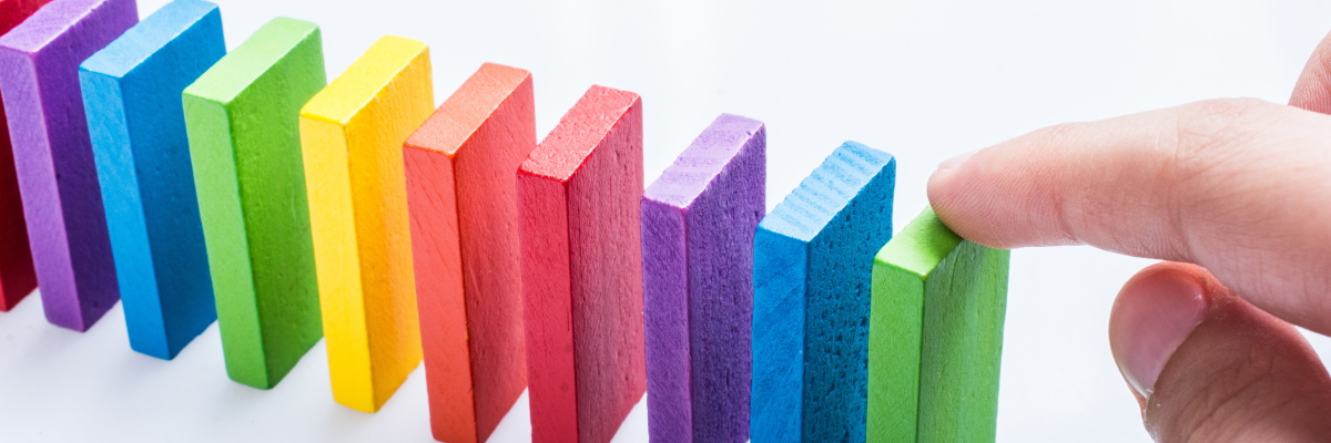 A row of colourful domino shapes, with a hand entering the right of the image, about to topple them