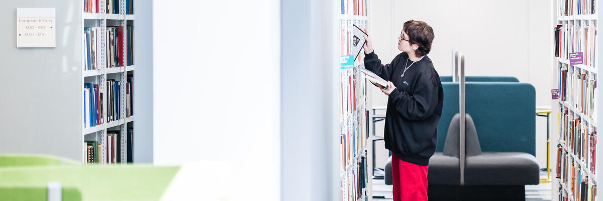 Someone selects a book from a library shelf 