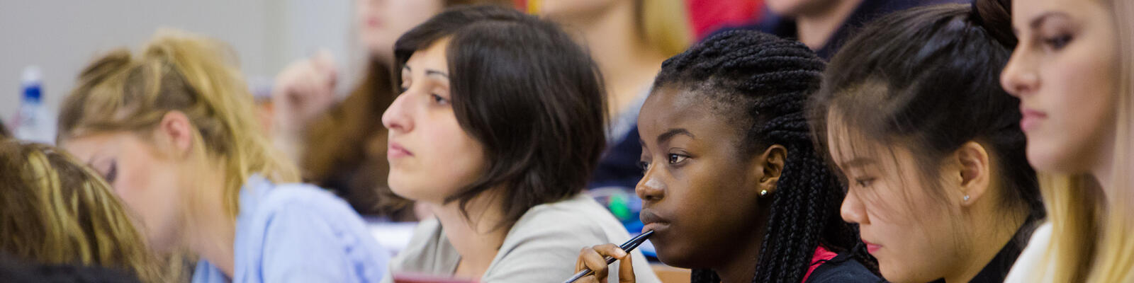 Group of students sat in a lecture theatre, looking to the left of the image.