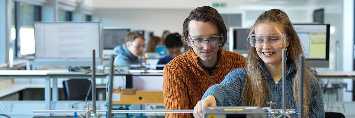 Two students sit at a bench in a teaching laboratory working on an electronics experiment.