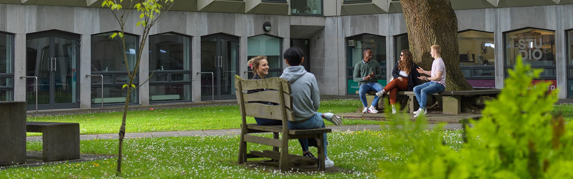 Students sit on benches in leafy gardens in summer