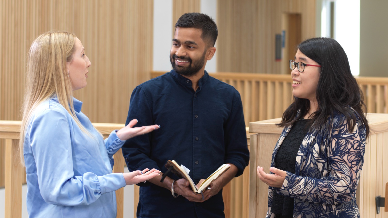 Three people talk in the Management School atrium.