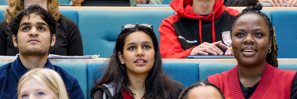 Students sat on a row of blue chairs in a lecture theatre