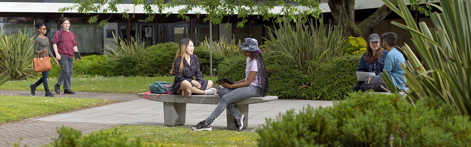 Students sitting on a stone bench chatting in an outdoor quad, surrounded by greenery