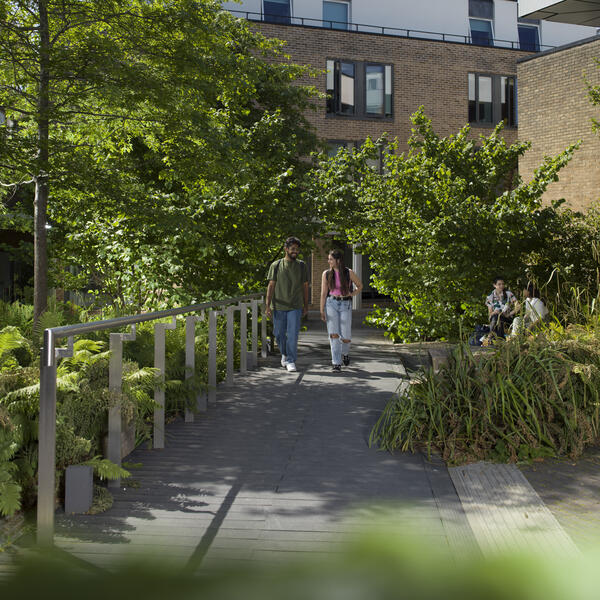 Two students walking through campus surrounded by trees